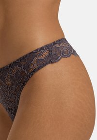 Dunne grijze strings met een bloemenpatroon. Voorzien van golvende randen en een doorschijnende textuur. Elastische tailleband voor een snugge pasvorm.
