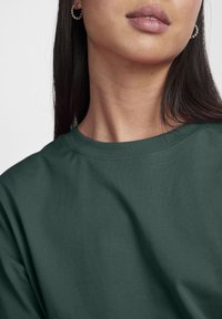 Camiseta de color verde oscuro fabricada con algodón suave, con un escote redondo y mangas cortas, sin patrones ni acentos visibles.