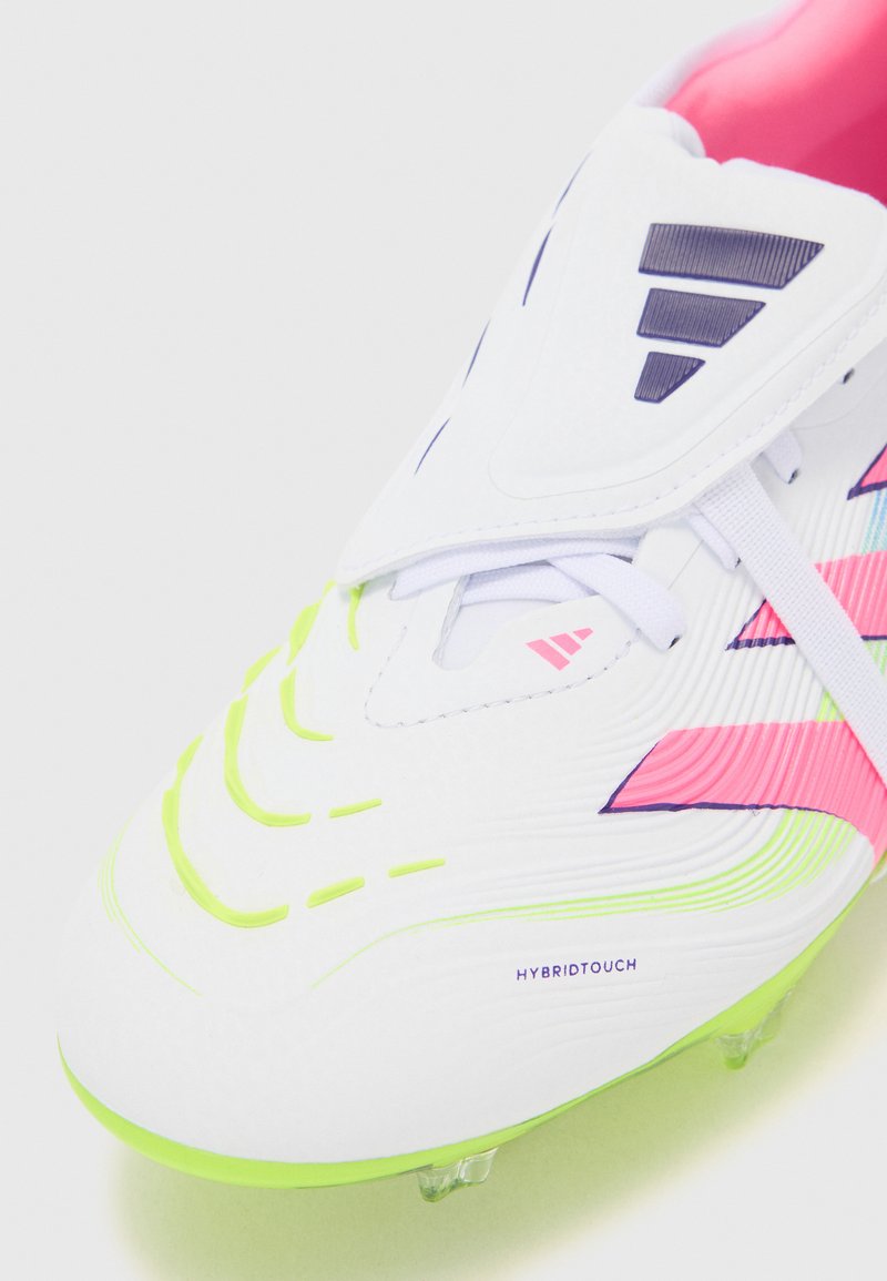Botas de fútbol blancas con acentos en rosa y verde. Presentan un upper texturizado, una marca prominente y una suela flexible con tacos visibles.