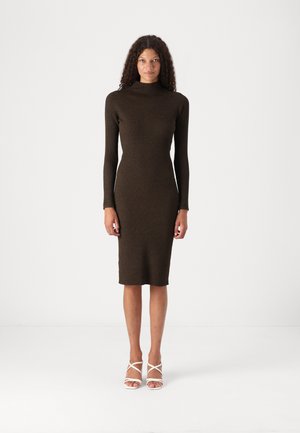 Knitted, form-fitting brown dress with long sleeves and a high neckline, featuring a ribbed texture and knee-length cut. Strappy white sandals.