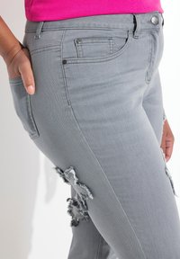 Šedé džíny z denimu s opotřebovanými efekty v oblasti kolen, s klasickým designem pěti kapes a jemnými detaily šití.