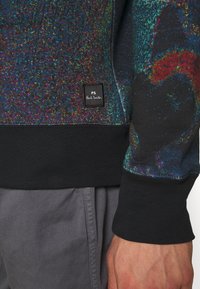 Černá mikina s texturovaným, mnohobarevným designem a žebrovanými manžetami. Obsahuje černou etiketu s logem "PS Paul Smith".