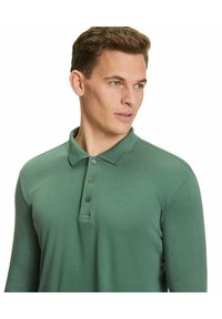 Langärmliges olivgrünes Poloshirt mit Kragen, dreiknöpfiger Knopfleiste und subtiler Textur. Figurbetontes Design mit glatter Oberfläche.