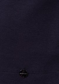 Close-up van een donker ribbelstof met een kleine ronde zwarte knop genaaid dicht bij de gestikte zoom.