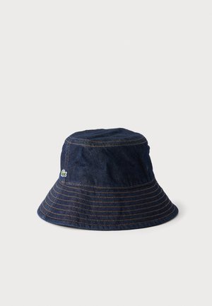 Donkerblauwe denim bucket hat met bruine stiksels en een klein groen-wit geborduurd logo aan de zijkant.