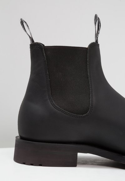 Black leather Chelsea boot featuring elastic side panels, a smooth texture, and a low, stacked wooden heel. Defined stitching detail at seams.