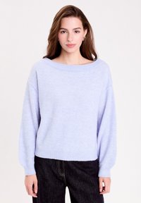 Sweater tricoté bleu clair avec un large col bateau, des épaules tombantes, des poignets et un ourlet côtelés. Tissu doux et texturé ; associé à un jean foncé.
