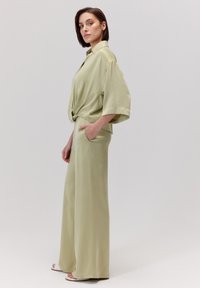 Jasnozielony, fakturowany satynowy strój składający się z luźnej bluzki z krótkim rękawem i detalem w postaci supełka w talii oraz szerokich spodni z nogawkami.