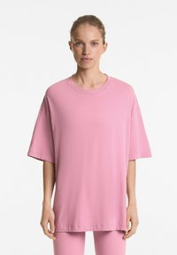 Tricou oversized roz deschis, cu decolteu rotund și umeri căzuți, fabricat dintr-un material moale din bumbac. Textură netedă, detalii minime de coasere.
