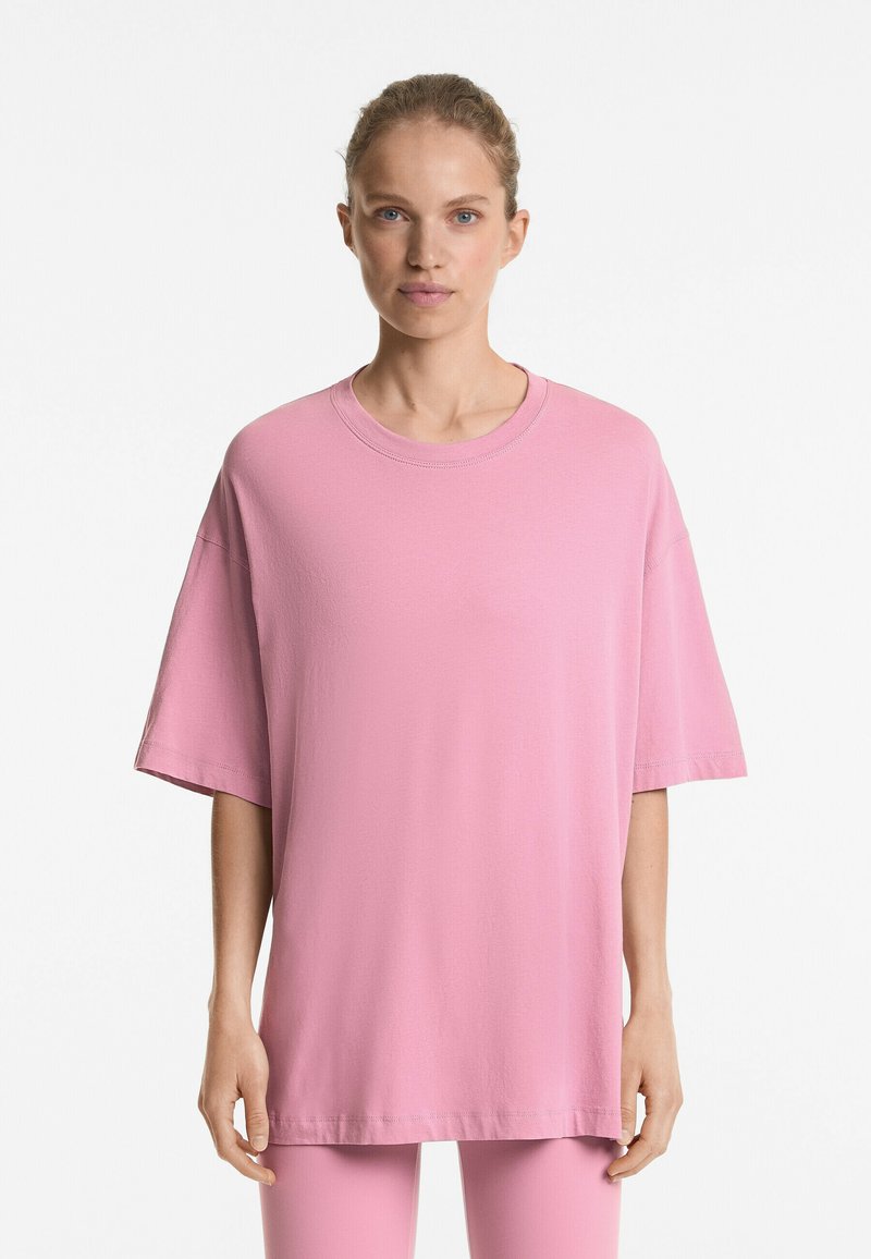 Tricou oversized roz deschis, cu decolteu rotund și umeri căzuți, fabricat dintr-un material moale din bumbac. Textură netedă, detalii minime de coasere.
