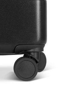 Hard-shell black suitcase featuring a textured finish and two black, rounded wheels for mobility. Zipper closure at the top.