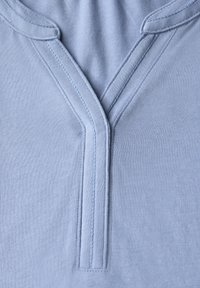 Světle modrá bavlněná tkanina s návrhem do V a plochým šitím, s hladkou texturou. Jednoduché, minimalistické detaily kolem výstřihu.