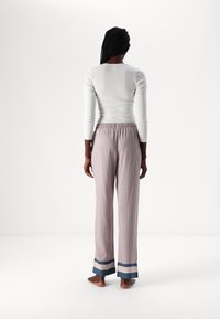 Witte lange mouwen top met een slimfit ontwerp, gecombineerd met lichte gestreepte pyjamabroek met blauwe en crèmekleurige boorden.