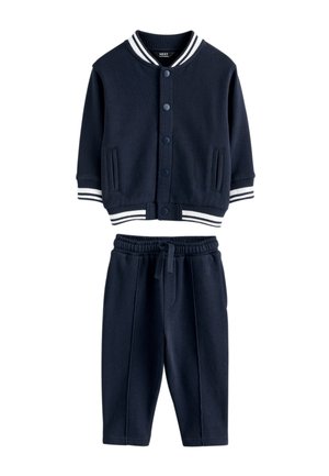 Veste bleu marine pour tout-petit avec poignets et taille côtelés à rayures blanches, associée à un pantalon à taille élastique avec cordon.