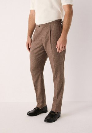 Brown tailored trousers with a textured fabric, front pleats, a button closure, and belt loops. Paired with black loafers.