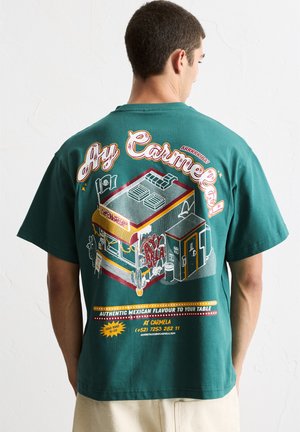 Green cotton t-shirt featuring a colorful graphic print of a Mexican food truck, with text and decorative elements in various colors.