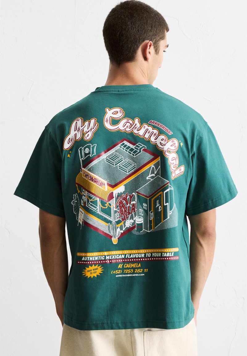 T-shirt en coton vert avec un imprimé graphique coloré d'un camion de nourriture mexicain, avec du texte et des éléments décoratifs dans diverses couleurs.