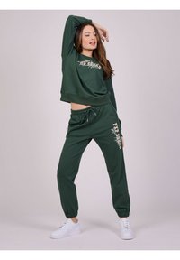 Groene cropped sweatshirt en bijpassende joggers van zachte stof. Kenmerken zijn een achterkant met trekkoord, geribde boorden en bedrukte tekst op de voorkant en zijkant.