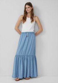 Gonna maxi di cotone blu chiaro con orlo a volant a strati e vita elastica. Abbinata a una canotta bianca aderente e sandali casual.