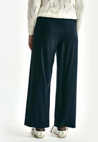 Wijde marineblauwe broek van zachte stof, met een gladde textuur en een elastische tailleband, gecombineerd met sneakers met zilveren accenten.
