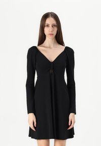 Vestido preto de mangas longas com decote em V e detalhe em forma de buraco na parte da frente. Feito de um tecido macio, com corpete justo e saia rodada.
