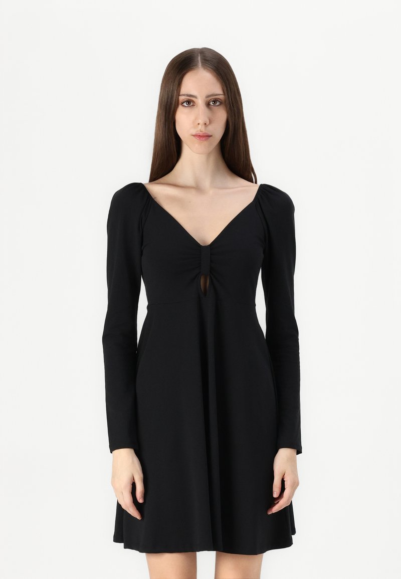 Vestido preto de mangas longas com decote em V e detalhe em forma de buraco na parte da frente. Feito de um tecido macio, com corpete justo e saia rodada.