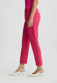 Rózsaszín, slim fit szabású nadrág, feltekert nadrágszárakkal és sima textúrával, fehér, hegyes orrú, sarokpántos magassarkú cipővel párosítva.