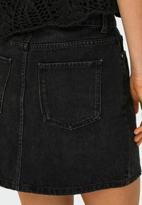 Zwarte denim rok met een klassieke snit, voor- en achterzakken en een iets rafelige zoom. De textuur is glad met een subtiele glans.