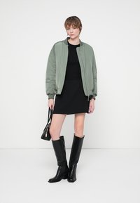 Světle zelená bomber bunda, černé šaty, černé kozačky po kolena a malá černá kabelka. Hladký materiál a přiléhavý střih.