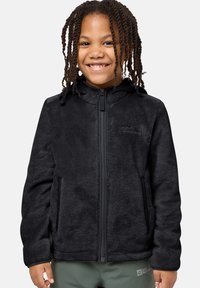 Schwarze Fleecejacke mit Reißverschluss, Kapuze und Seitentaschen; weiche Textur und stromlinienförmiges Design. Über grünen Hosen getragen.