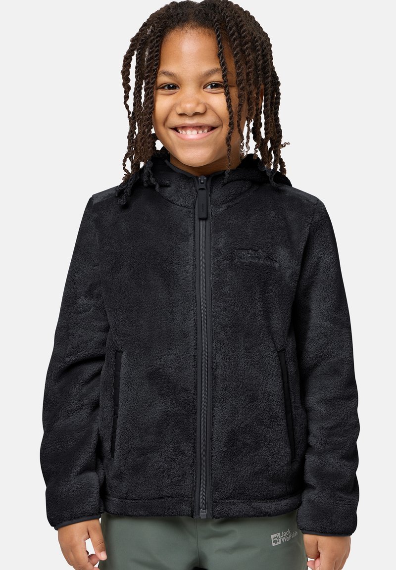 Schwarze Fleecejacke mit Reißverschluss, Kapuze und Seitentaschen; weiche Textur und stromlinienförmiges Design. Über grünen Hosen getragen.