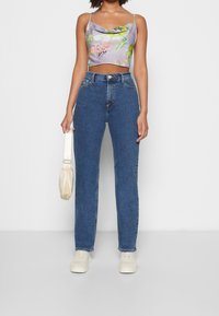 Top sin mangas y cortado en un suave tono púrpura con patrones florales, combinado con unos jeans de mezclilla azul de pierna recta y talle alto, y zapatillas blancas.