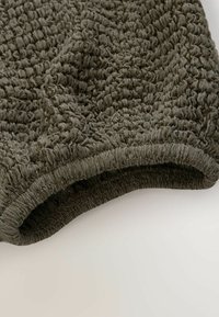 Gros plan sur un tissu texturé vert olive foncé avec un détail élastique froncé, montrant un tissage recueilli et extensible sur un fond clair.