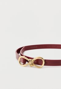 Bordowy skórzany pasek z złotą klamrą w kształcie nieskończoności. Pasek jest cienki i gładki, posiada wytłoczone litery marki po wewnętrznej stronie.