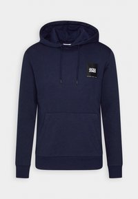 Námořnická modrá mikina s kapucí vyrobená z měkké tkaniny, která má přední klokanku, kapuci na šňůrku a černou čtvercovou nášivku loga na prsou.