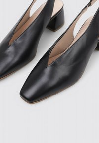 Tacones slingback de cuero negro con punta cuadrada, tacón bajo y diseño recortado, presentando una textura suave y detalles de costura mínimos.