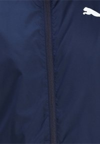 Navy windbreaker jacket with a smooth texture, full zipper, and a white logo accent on the chest. Lightweight and water-resistant material.