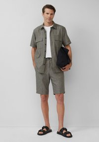 Grijs overhemd met korte mouwen en knopen, wit t-shirt, bijpassende shorts en zwarte sandalen. Beschikt over twee borstzakken en een eenvoudig ontwerp.