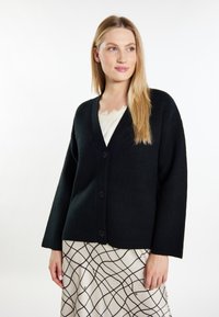 Schwarze, gemütliche Strickjacke mit V-Ausschnitt, langen Ärmeln und drei Knöpfen auf der Vorderseite, ergänzt durch ein Top mit cremefarbener Spitzenborte darunter.