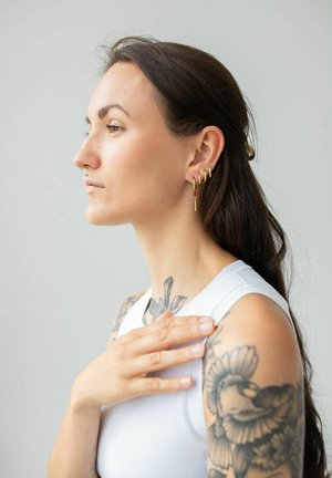 Gold-tone earrings with red accents, featuring a spiraled design. The subject has long hair and visible tattoos on the arm and shoulder.