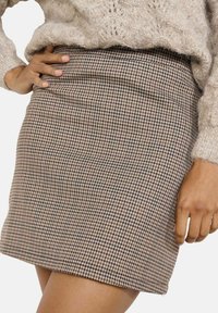 Checkered mini skirt in brown and cream hues, featuring a fitted design and smooth texture. Accented with a subtle pattern, it sits at the waist.