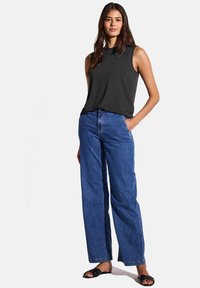 Svart ärmlös topp med rund halsringning, matchad med vida blå jeans. Modellen bär svarta slidesandaler; tygkänslan ser slät ut.