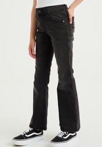 Čierne rozšírené rifle z denimu s päťvreckovým dizajnom, zapínaním na gombík, jemným vyblednutím a kombinované s čiernymi a bielymi teniskami.