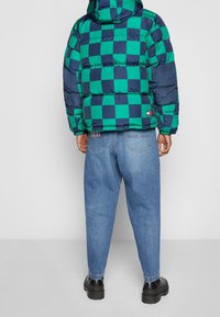 Puffer jacket in green and navy checkered pattern with hood; paired with light blue jeans and black chunky-soled boots.