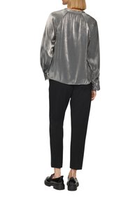 Zilverkleurige metallice blouse met geplooide schoudernaden, gecombineerd met zwarte tapered broeken en zwarte plateau schoenen, wat een slanke silhouet benadrukt.