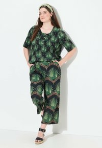 Zwart outfit met groene palmbladeren patronen; losse top met knopen en korte mouwen, gecombineerd met bijpassende wijde broek. Zwarte sandalen.