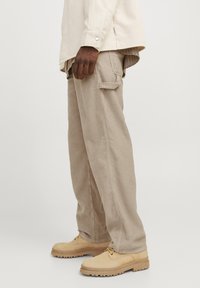 Beige corduroy cargo pants with a relaxed fit, featuring side pockets, a loop detail, and paired with light tan lace-up shoes.