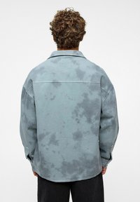 Vervaagde blauwe denim overshirt met een relaxte pasvorm, grote kraag en knoopsluiting op de mouwen, met een vlekkerig waspatroon.