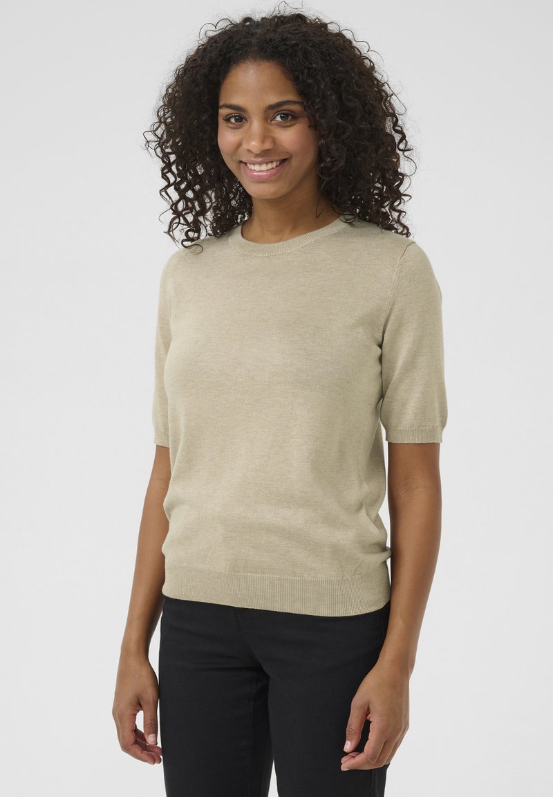 Pull à manches courtes, couleur kaki clair, fabriqué en tissu doux. Présente un col rond et un ourlet côtes, associé à un pantalon noir.