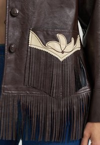 Smeđa kožna jakna s resama. Ima kremasti ukrasni remen i ukrasne šavove. Zatvaranja su tamni gumbi.